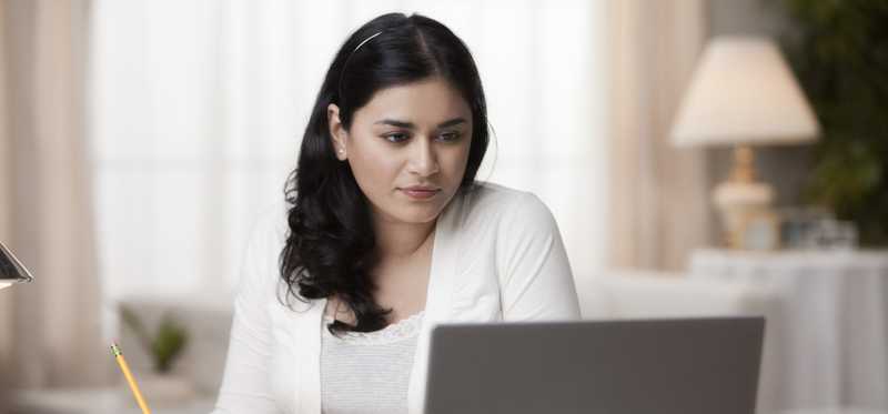 Person at desk is looking at laptop and writing notes.