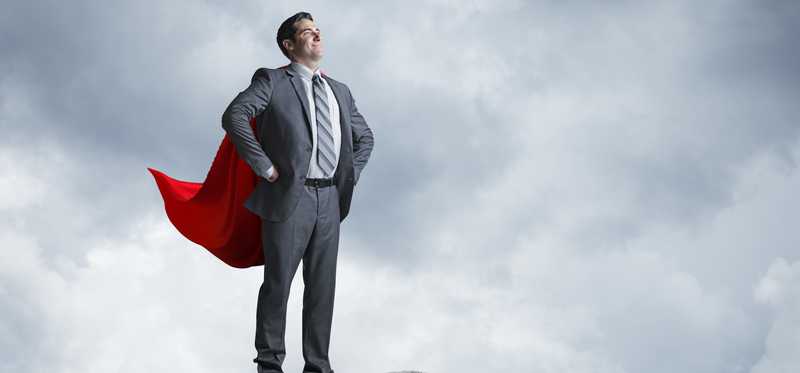 Businessman in superhero cape is standing on cliff overlooking city
