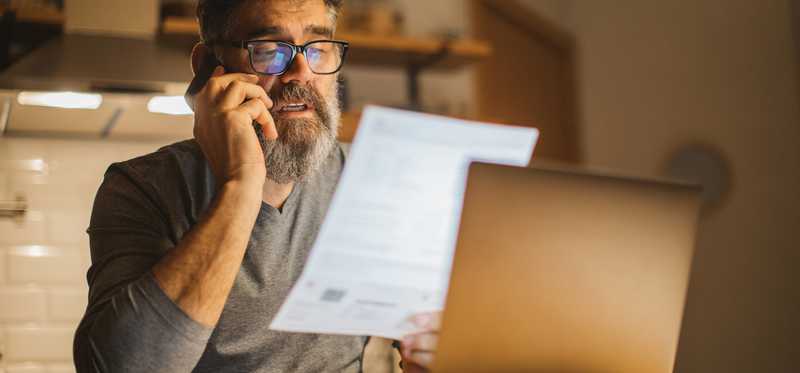 Person sitting in kitchen while looking at paperwork and making phone call.