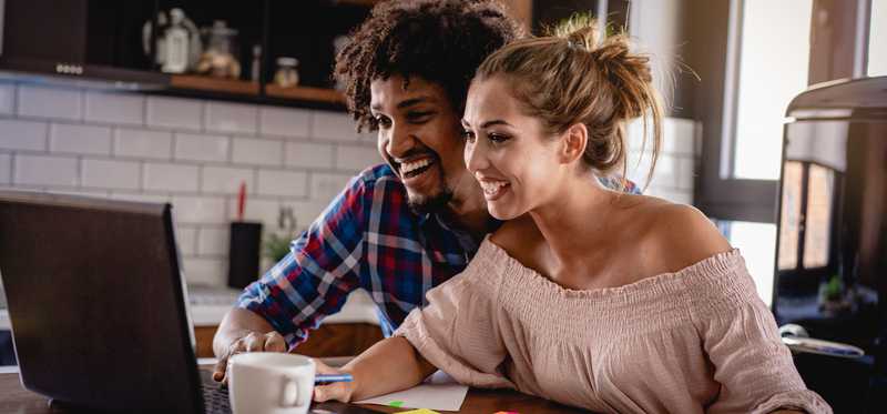 Two smiling people in kitchen looking at computer screen.