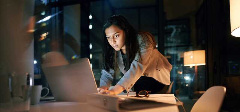 Woman standing over desk scrolling on laptop