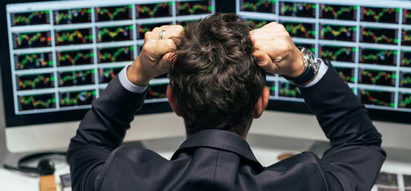 Frustrated investor looking at multiple screens and putting hands to head.