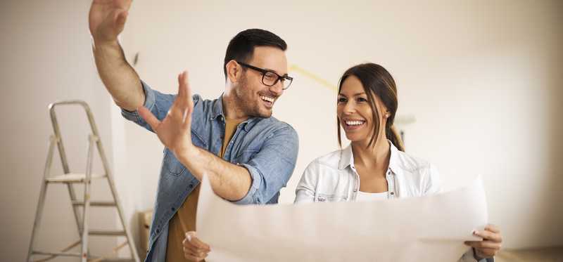 Two people smiling while looking at blueprints for remodeling a home.