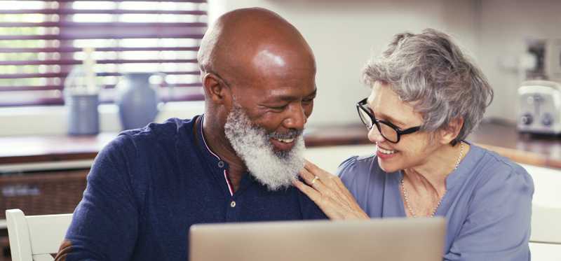 Two smiling people using laptop in kitchen.