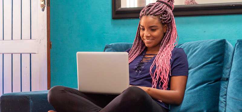 Smiling person sitting cross-legged on couch and using laptop.