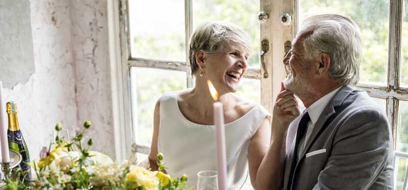 Two people smile at each other while seated at a table during a formal and festive celebration.