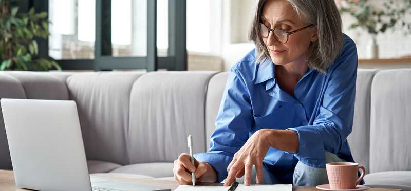 Smiling person writing note in front of laptop.