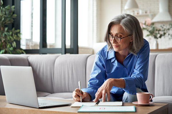 Smiling person writing note in front of laptop.