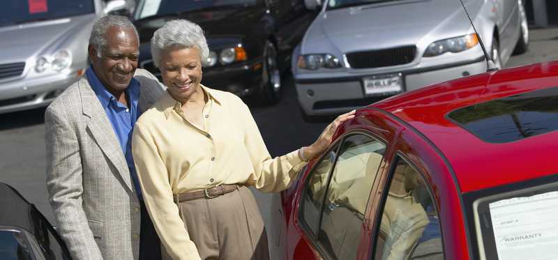 Two people smiling while standing next to car.