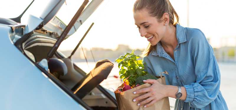 Smiling woman putting bag of groceries in car
