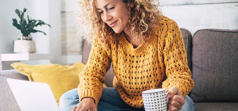 Smiling person with coffee mug and laptop.