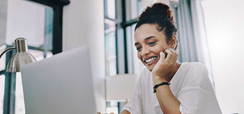 Smiling person with hand on chin and looking at laptop.
