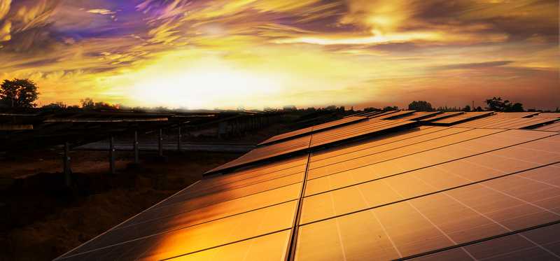 Solar panels on a rooftop with the sun setting in the background.