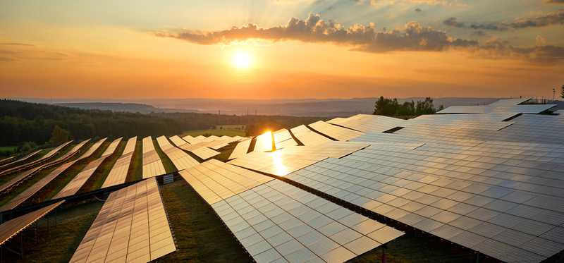 Solar panels with the sun setting in the background.