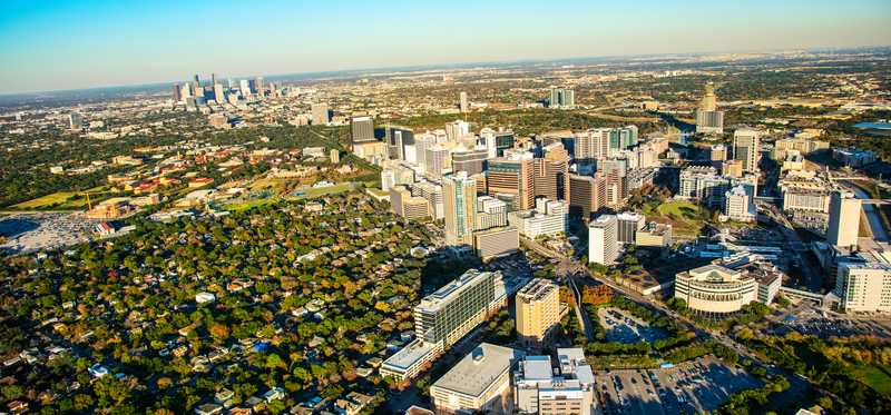 A high aerial shot showing downtown Houston, Texas, with more tall buildings in the far background.