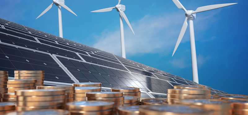Stacks of coins with wind turbines and solar panels in the background.