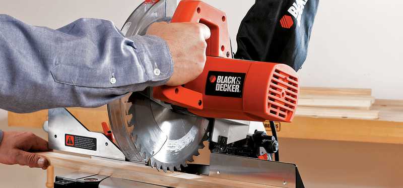 Person using a Stanley Black & Decker saw to cut a piece of wood.