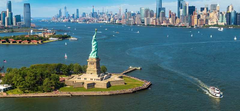 An aerial shot of the Statue of Liberty and New York Harbor and some of the city.