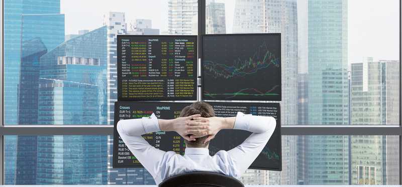 Man sitting at desk with hands behind head looking at multiple computer screens