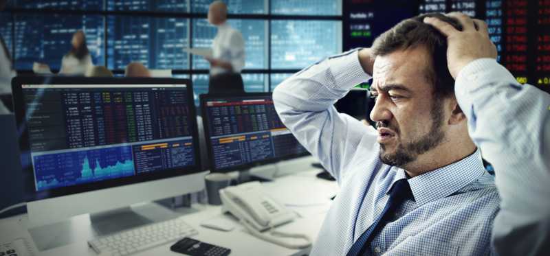 A trader looking at monitors in dismay with hands on head.