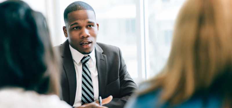 Suited businessperson talking to two clients.