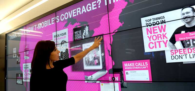 Person pointing at a coverage map hanging on the wall of a T-Mobile store.