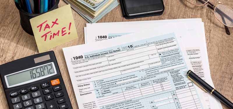 Tax documents on a desk with a pen, calculator, and note that says "Tax time!"