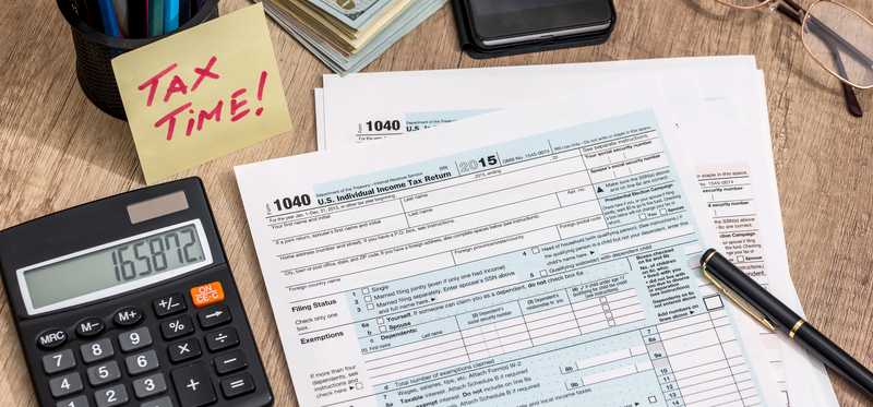 Tax documents on a desk with a pen, calculator, and note that says Tax Time.
