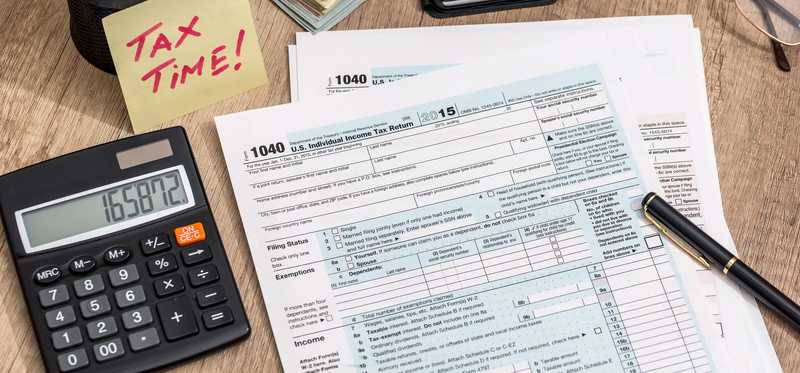 Tax documents on a desk with a pen, calculator, and note that says Tax Time.
