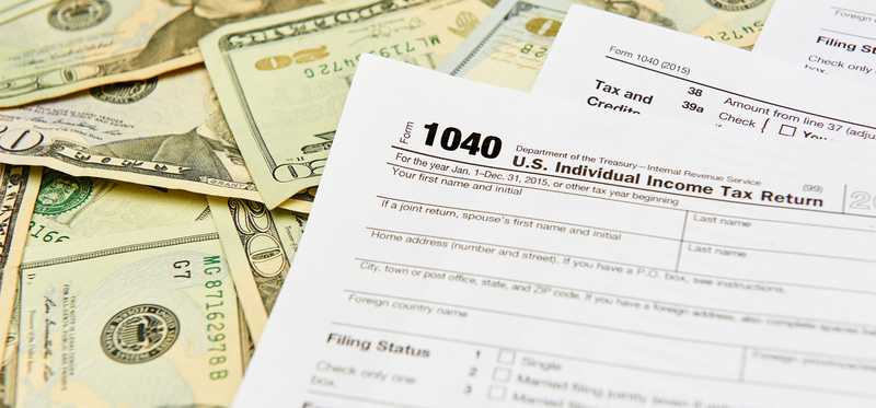 Tax form 1040 on top of a pile of twenty dollar bills.