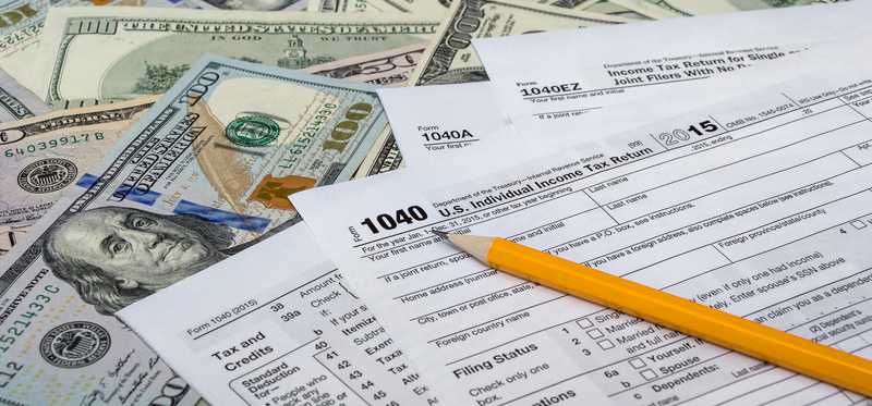 Tax forms lay atop hundred dollar bills.