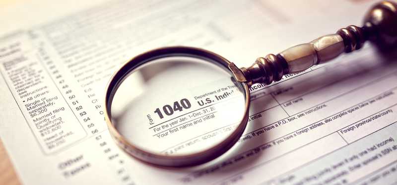 A magnifying glass sits on top of a 1040 tax form.