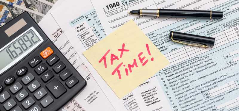 Tax forms and calculator with Post-it note reading Tax Time!