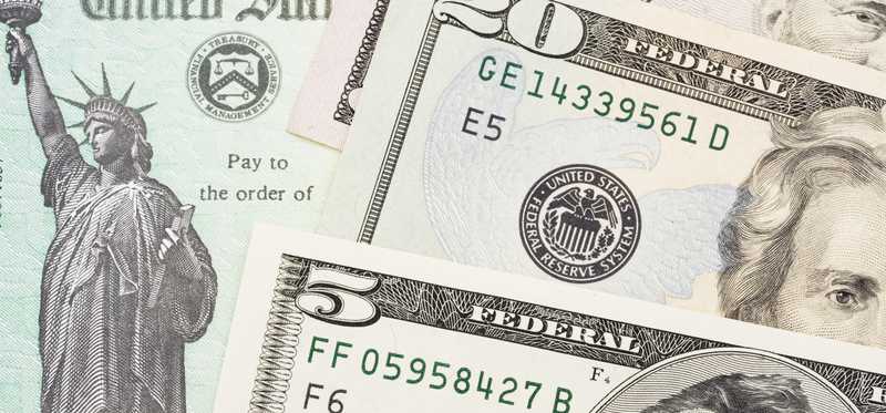 Tax refund check with cash money lying on top of it.