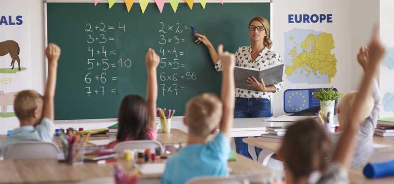 A teacher at the front of a classroom full of kids.