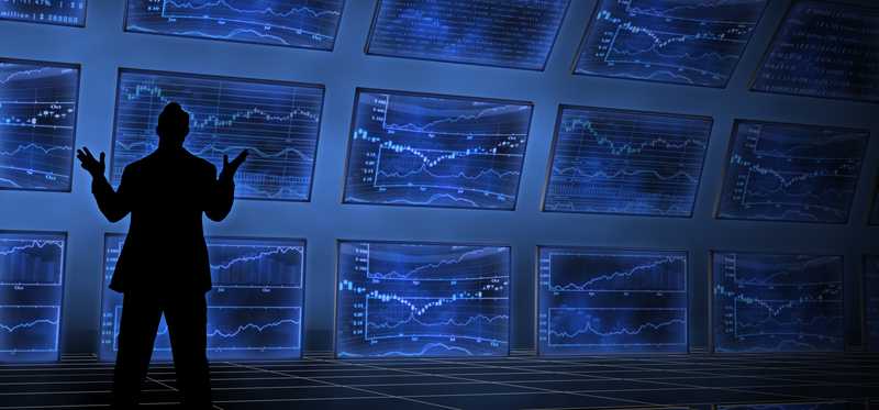 Man standing in front of a wall of tv screens with market graphs.