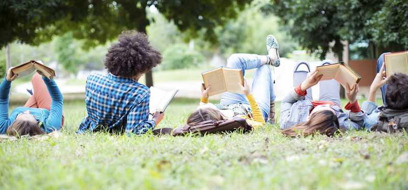 Teenagers reading and lounging in the grass.