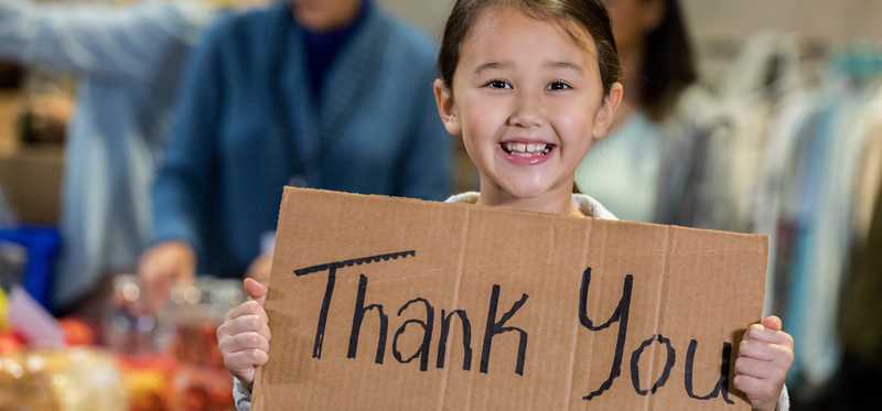 Child holds up cardboard sign saying Thank You.