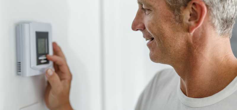 Smiling person adjusting a thermostat.