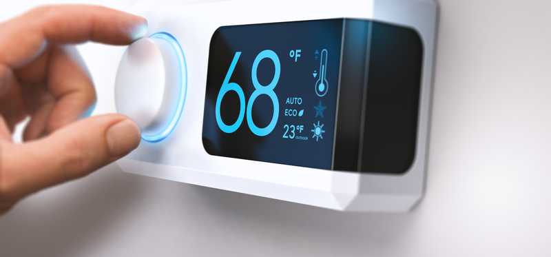 A thermostat with a hand about to adjust it
