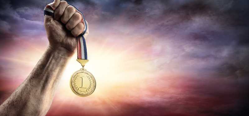 A hand hoists up a gold medal into the air.