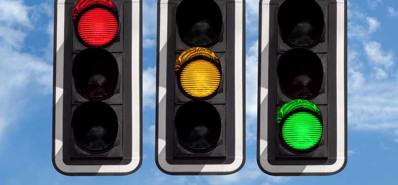 Three traffic lights with one each lit up in red, yellow, and green.