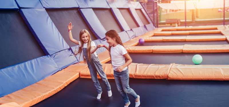 Two girls bounce around on an indoor trampoline.
