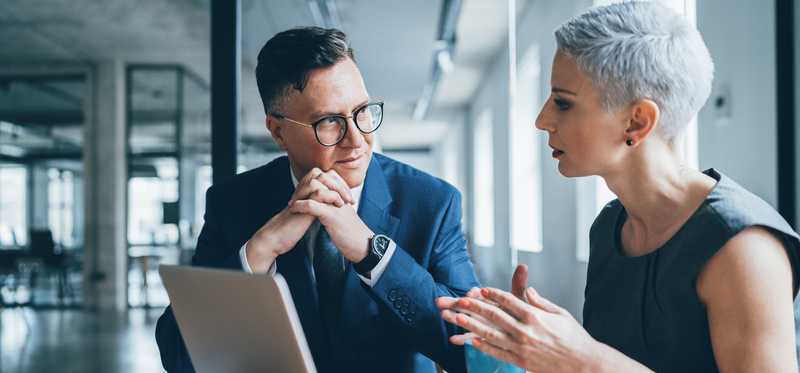 Two businesspeople talking in front of a laptop.