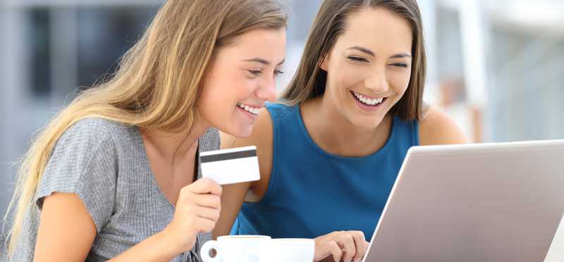 Two young girls using a laptop while smiling holding a credit card.