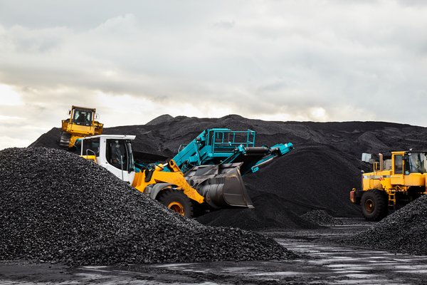 Four industrial trucks and machines in a mining area with piles of raw material