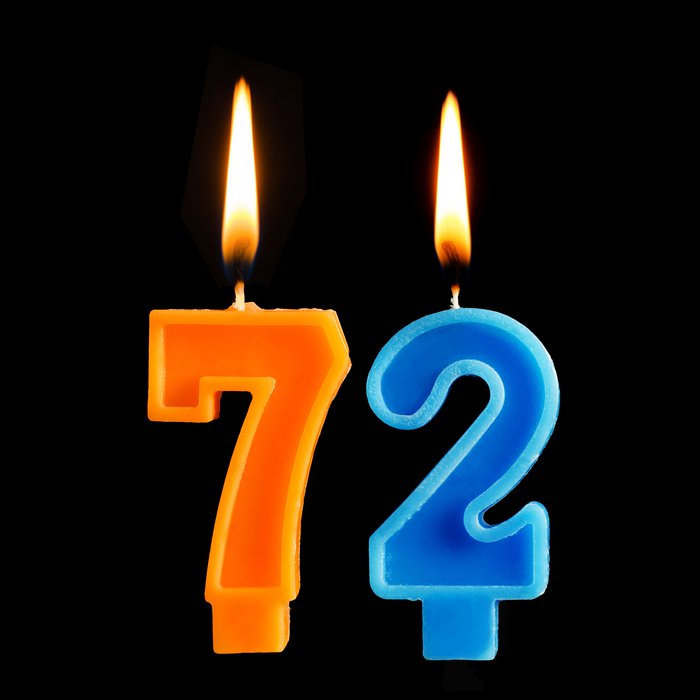 Two lit birthday candles reading 72 against black background