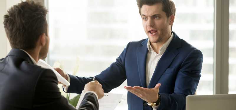 Two men in suits arguing across a desk.
