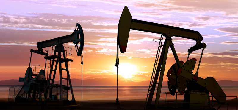 Two oil pumpjacks operating with sun setting in the background