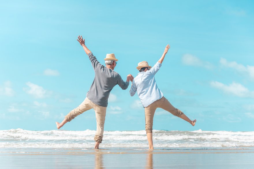 Two older men on beach holding hands with arms in the air